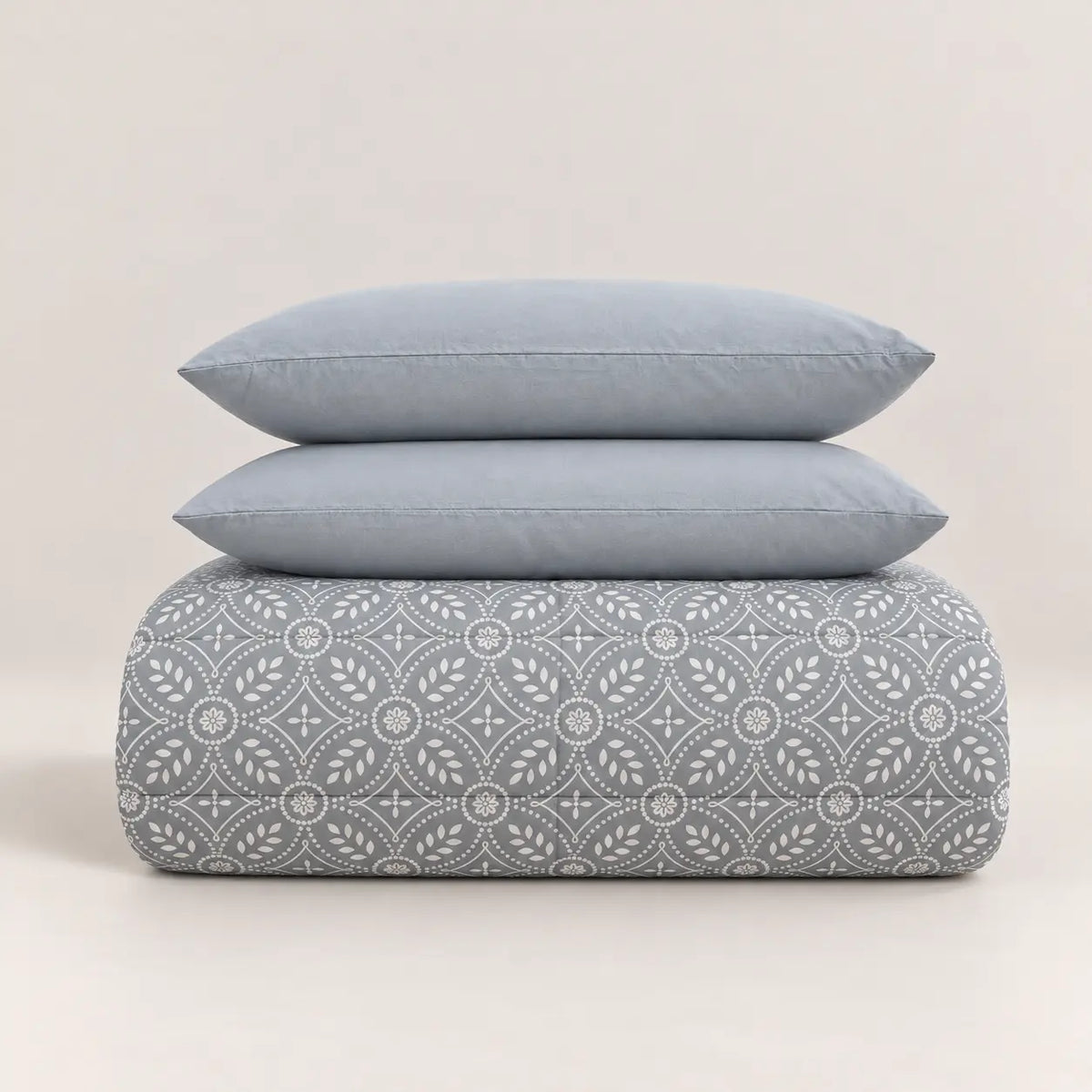 Detalle que resalta la bonita combinación entre el tejido estampado del edredón y la textura lisa y suave de las fundas de almohada azul grisáceas.