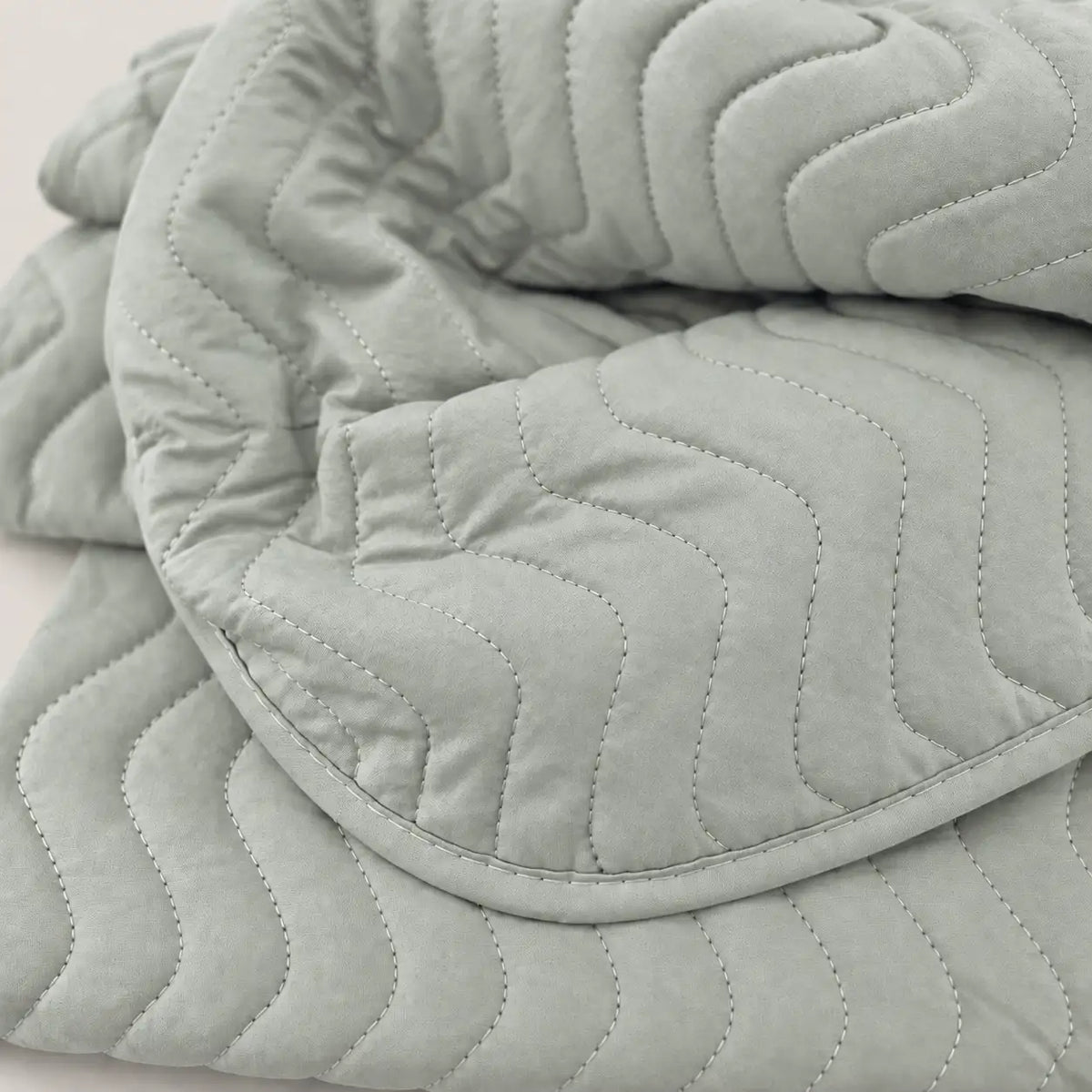 Primer plano del cosido reforzado con patrón zig zag sobre la microfibra lisa de alta calidad en tono verdoso.